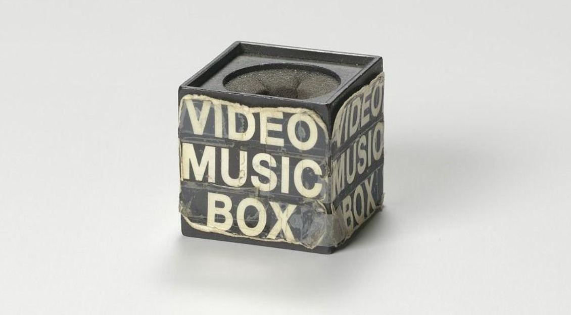 A black microphone box used on the television show Video Music Box, featuring white text wrapped around it that reads “Video Music Box” in a bold, graphic style. The box shows signs of wear and tear, reflecting its use. This microphone box, dating back to around 1988, is part of the collection at the Smithsonian National Museum of African American History and Culture.