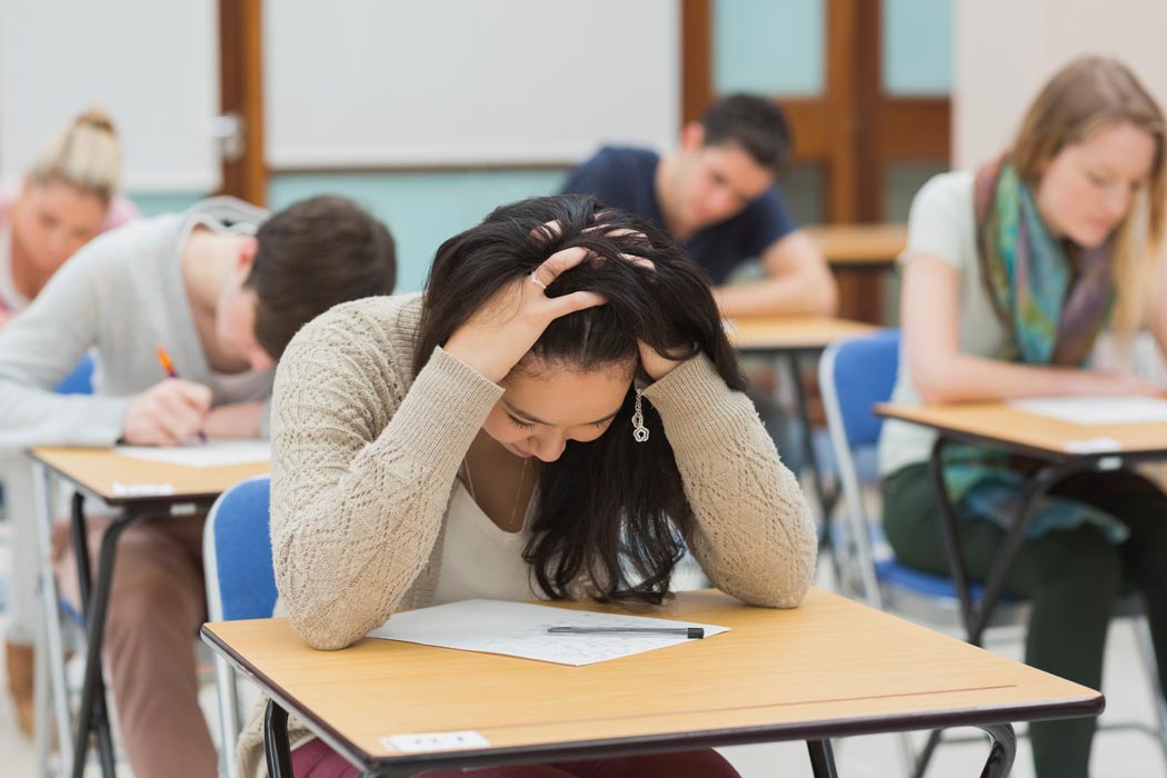 A student puts her head in her hands as she looks down at the assignment in front of h