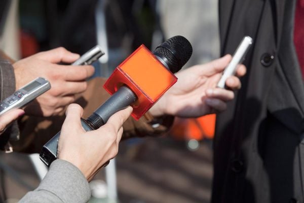 Reporters hold old voice recorders and a microphone to their subject