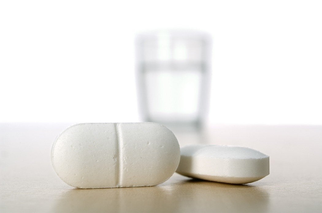 Close-up of two pills with a blurred glass of water in the background