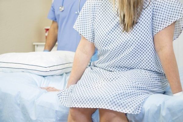 A woman in a hospital gown sitting on a hospital bed with a doctor behind her