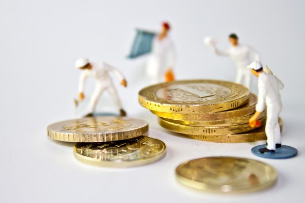 miniature people standing on around a stack of coins