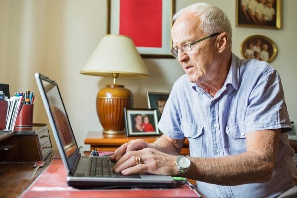 An elderly man typing on a laptop