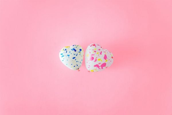 Two heart-shaped balloons against a pink background