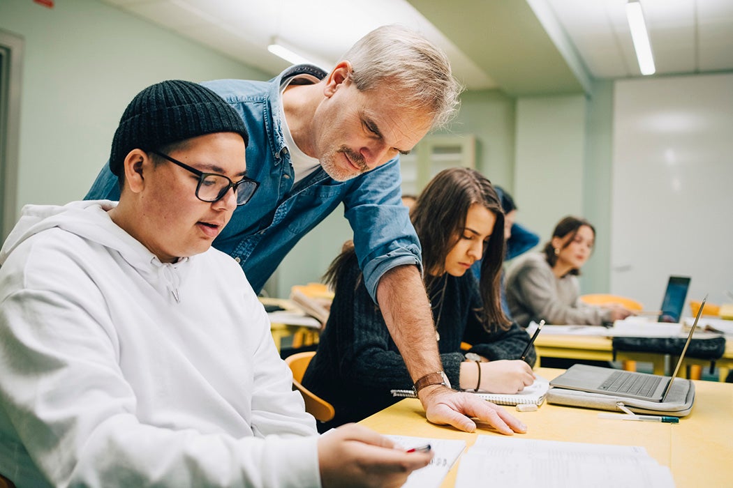 Male teacher assisting student at desk in classroom