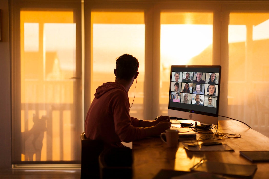 A young man looks out his balcony window, ignoring his Zoom call