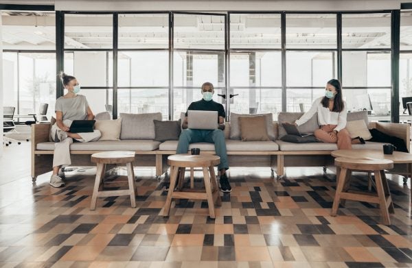 Businesspeople working and maintaining social distance on a sofa in a modern office