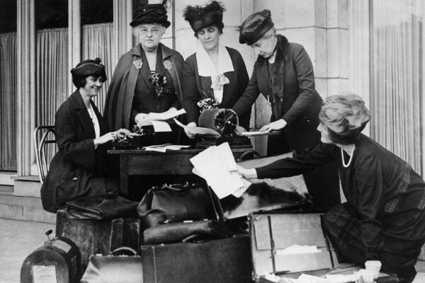 League of Women Voters representatives gather around a table on a sidewalk while writing and mimeographing news releases to hand out at train stops en route to the Democratic Convention.