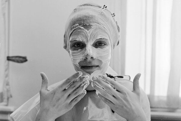 A woman gently applying skin cream to her face with the tips of her fingers, circa 1955