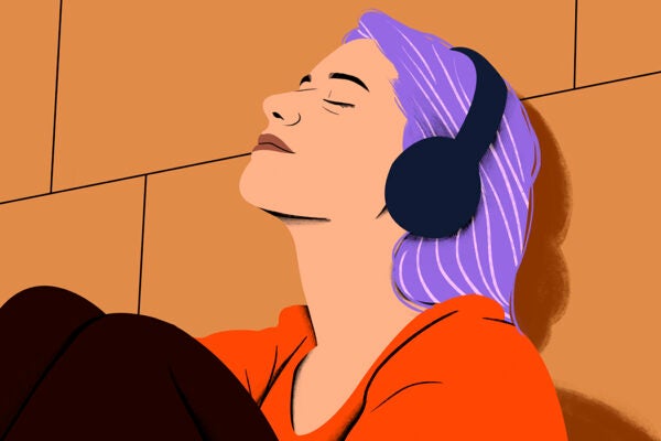 Woman with purple hair enjoying music on black headphones with eyes closed against an orange background