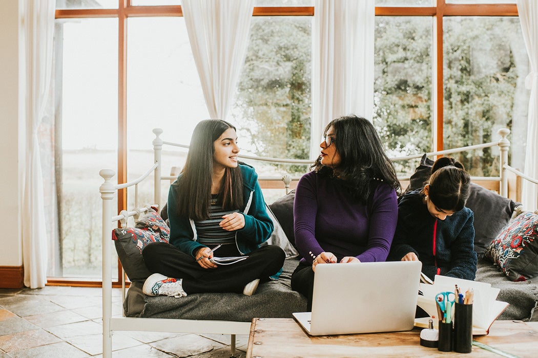 A mom looks at the teenage friend of her daughter and listens intently to her explaining an idea during a homework session.