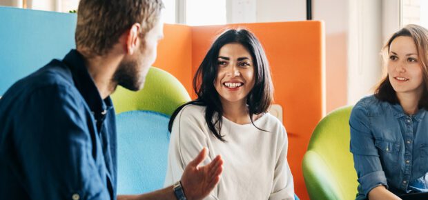 A meeting between three team leaders sitting in colorful chairs in a modern office environment.