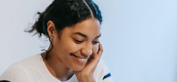 Smiling young ethnic woman working distantly on laptop and talking on smartphone