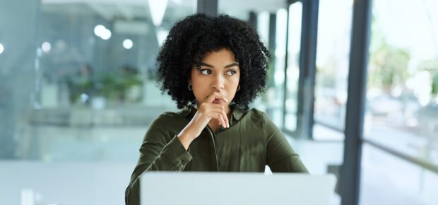 Shot of a young businesswoman looking thoughtful while using a laptop in a modern office